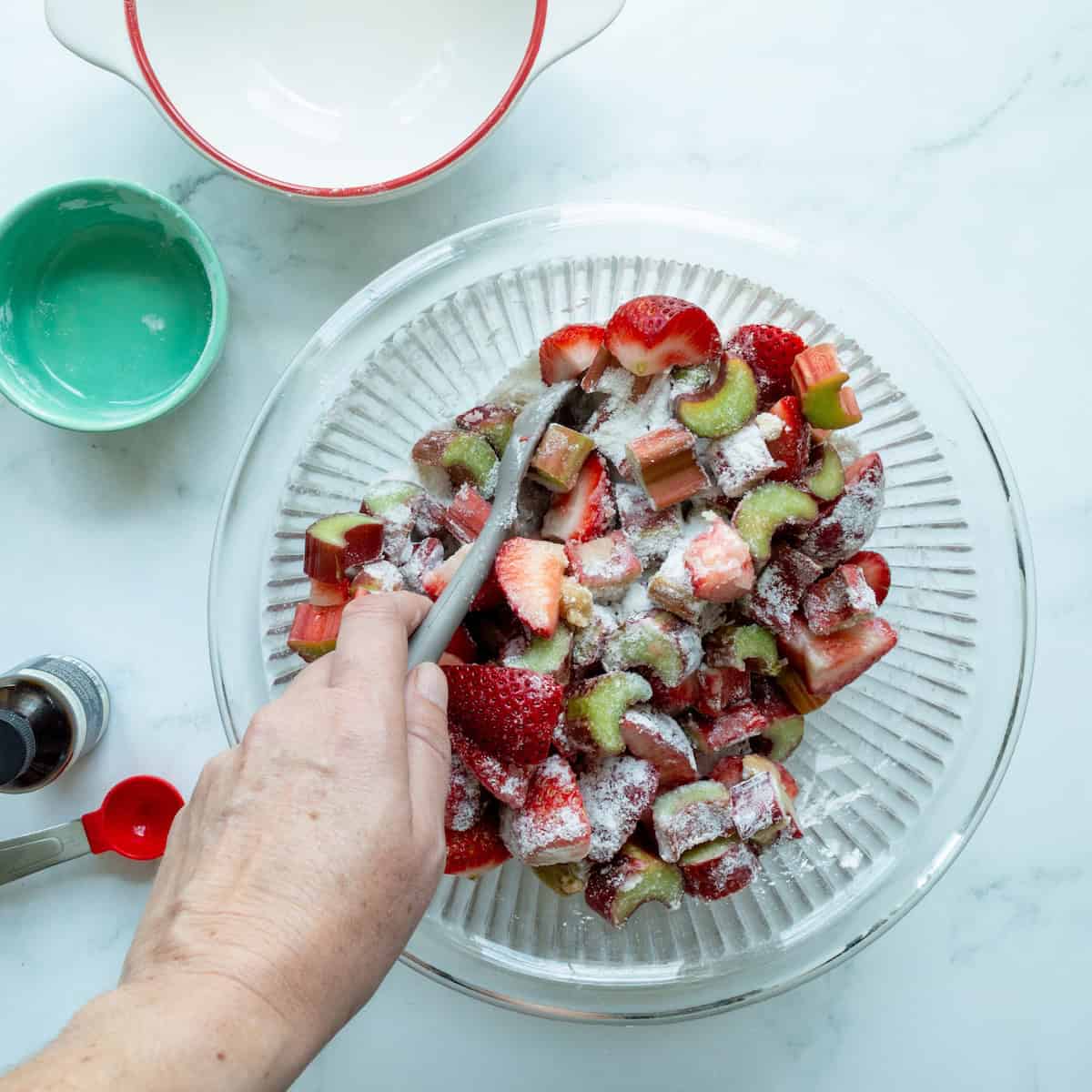 Stirring together the filling for strawberry rhubarb pie in a glass bowl.