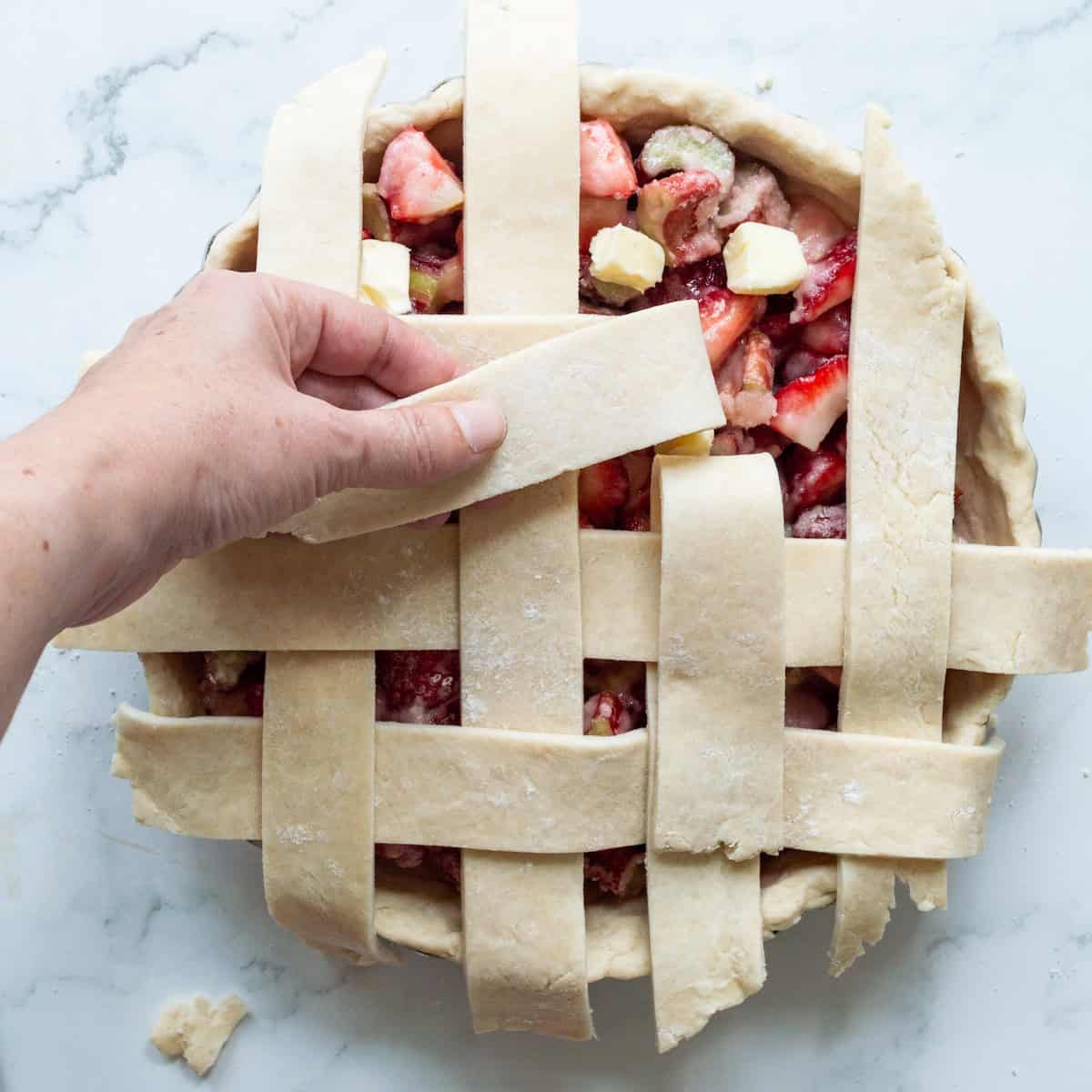 Weaving pie dough in a lattice design on a strawberry rhubarb pie.
