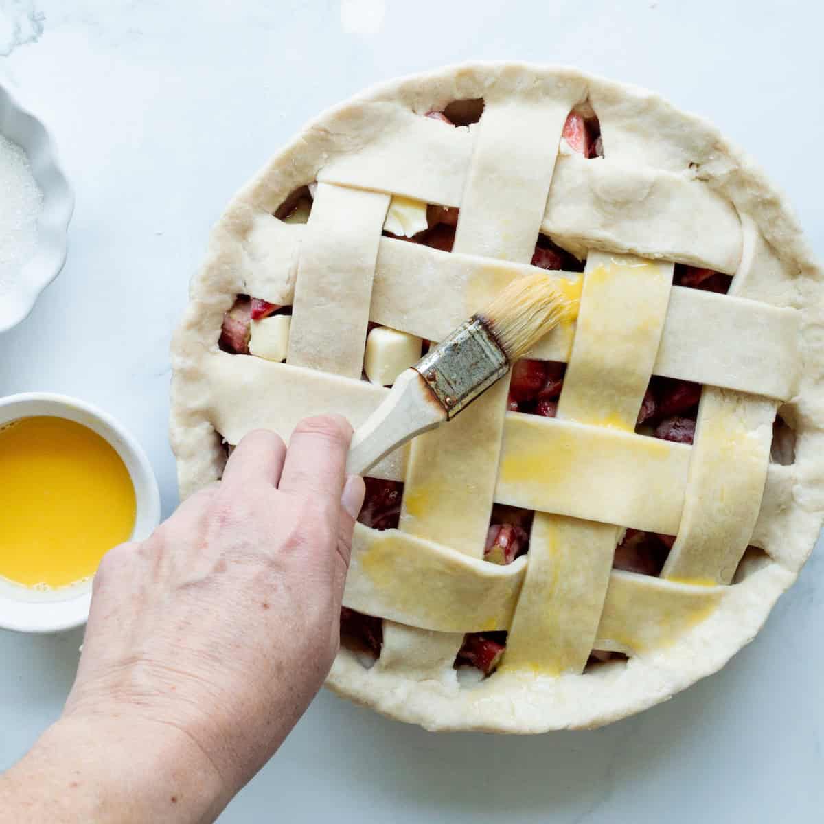 Brushing egg wash onto the lattice crust of a strawberry rhubarb pie.