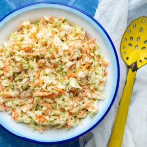 Creamy Southern coleslaw in a blue rimmed enamel bowl with a yellow enamel spoon on the side.