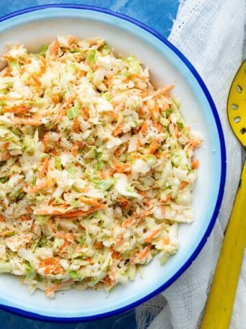 Creamy Southern coleslaw in a blue rimmed enamel bowl with a yellow enamel spoon on the side.