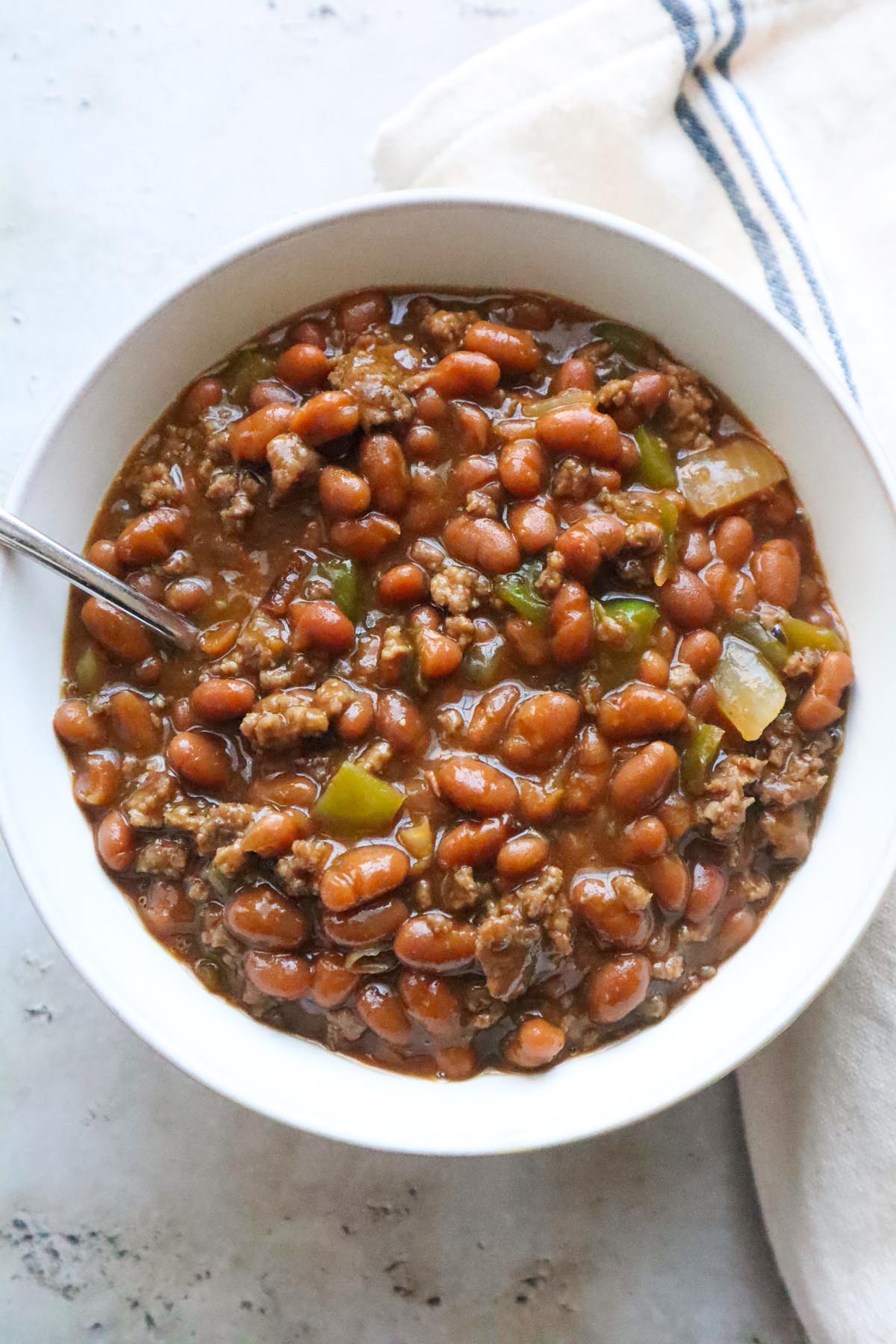 Close-up of bean and ground beef stew in a white bowl with a spoon.