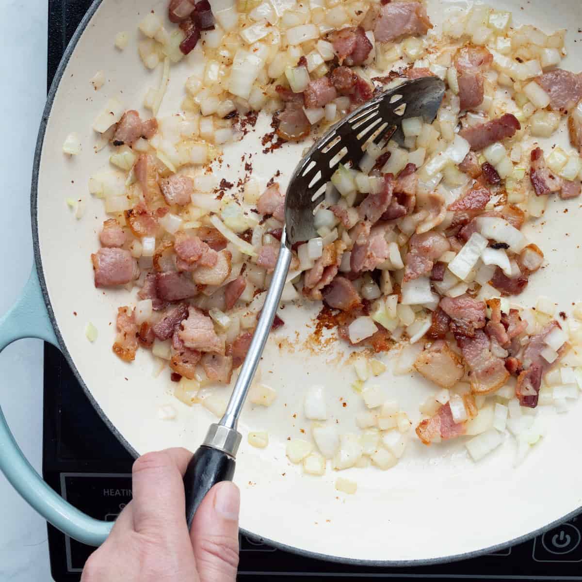 Sauteing bacon and onion in a large enamel pan.