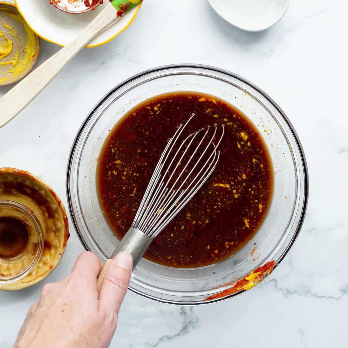 Whisking together the sauce for bbq baked beans in a clear bowl.