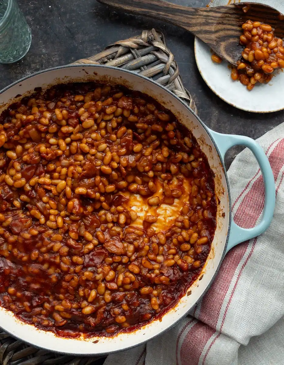 Baked beans in a skillet with rich tomato sauce and spices, served with a wooden spoon.