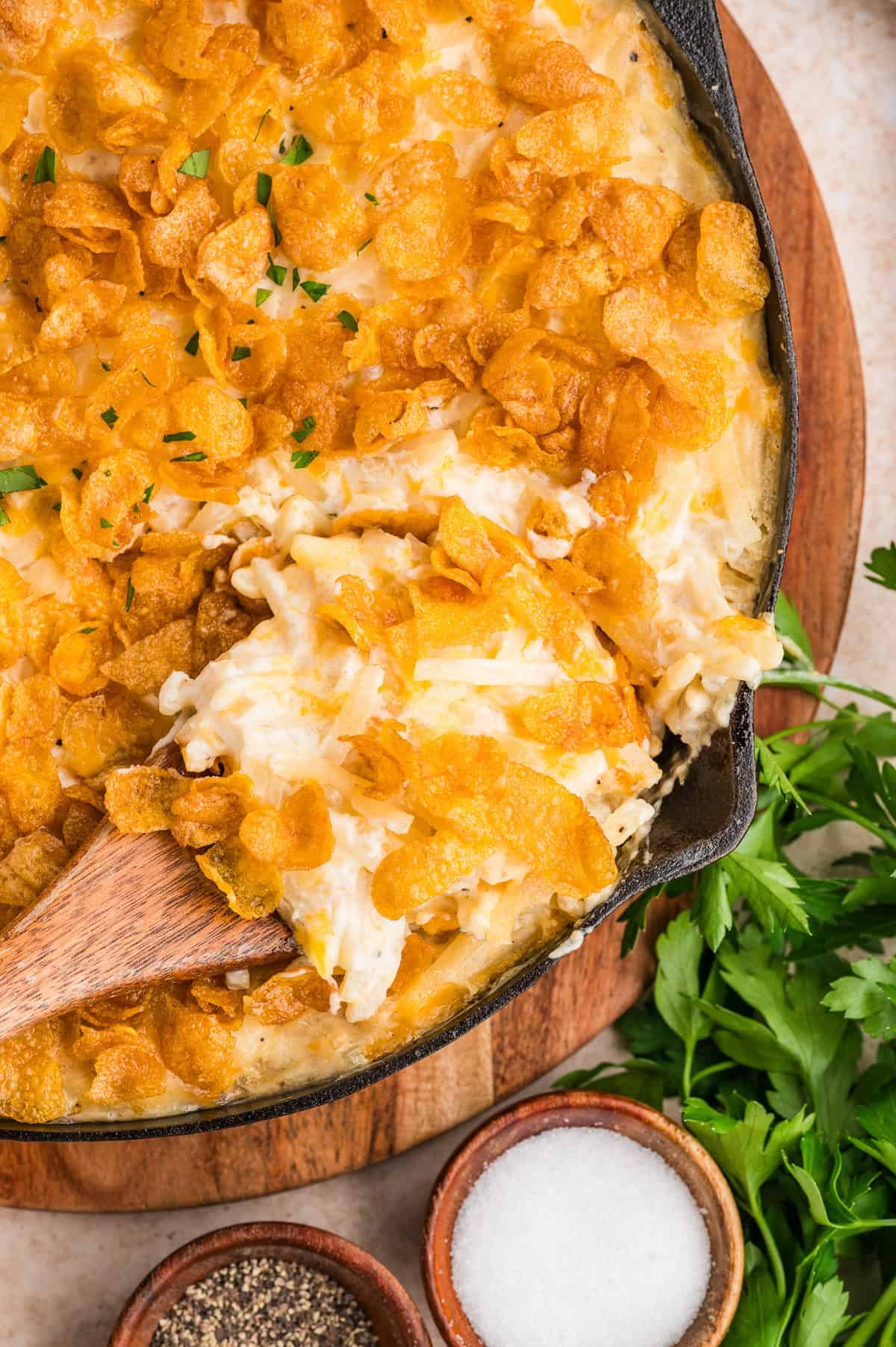 Cheesy potato casserole topped with crispy potato chips in a cast iron skillet, served with a wooden spatula.