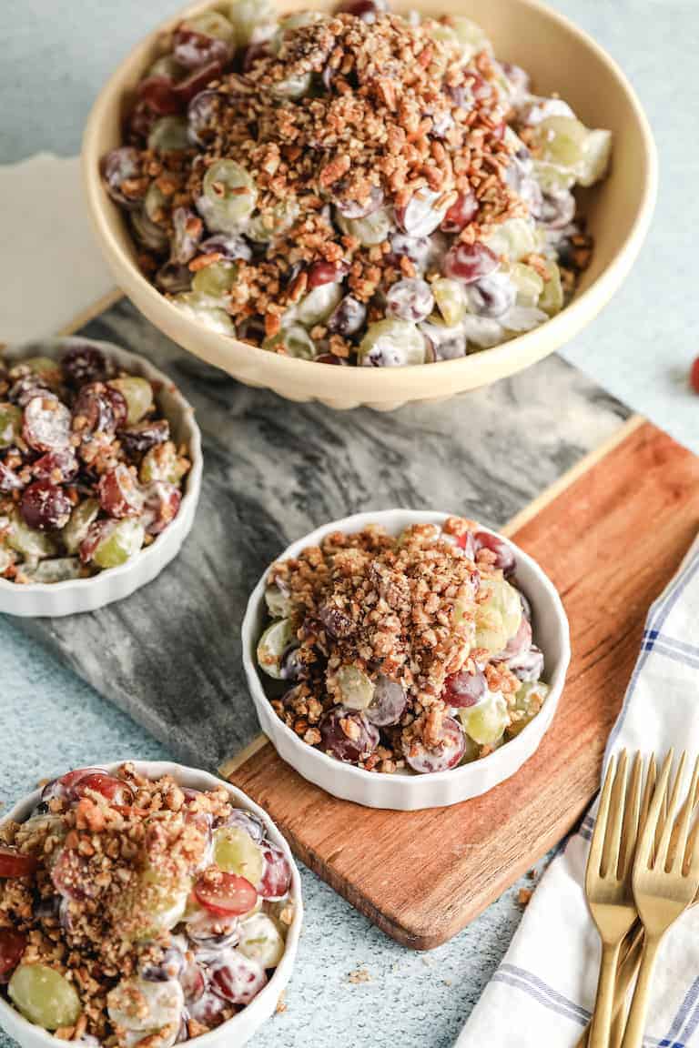 Creamy Southern grape salad served in a large yellow bowl and small white ramekins on a wooden cutting board.