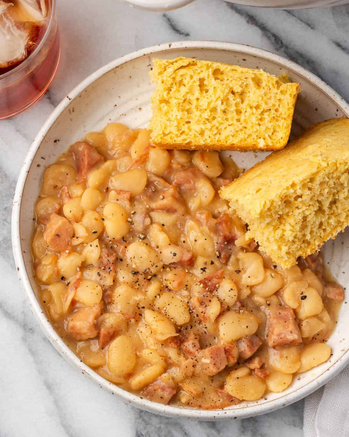 Creamy lima beans with ham served in a bowl with two pieces of cornbread on top.