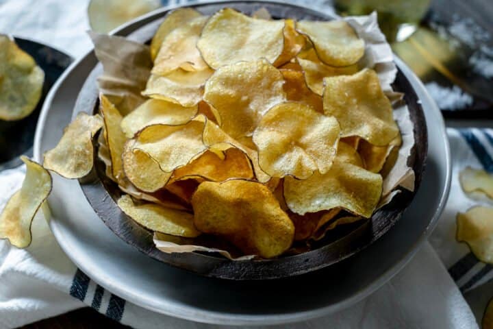 Homemade potato chips piled in a wooden bowl lined with parchment paper.