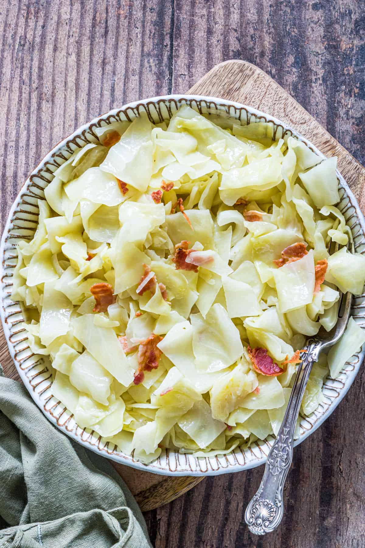 Creamy smothered cabbage with bacon pieces in a decorative bowl on wooden table.