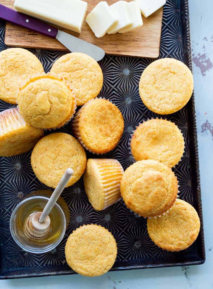 Golden cornbread muffins arranged on a serving tray with butter and honey on the side.