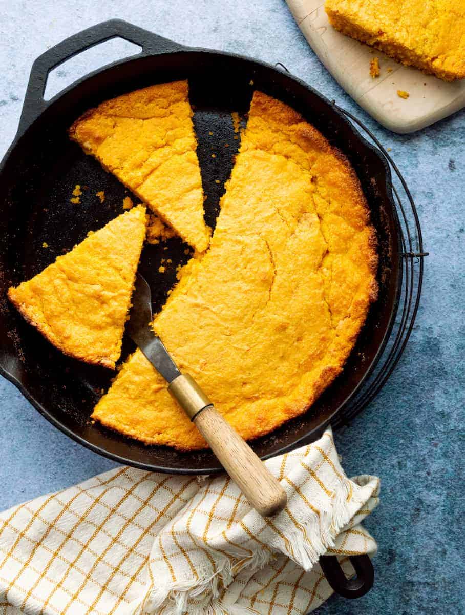 Sweet potato cornbread baked in a cast iron skillet with several slices cut and served with a pie server.