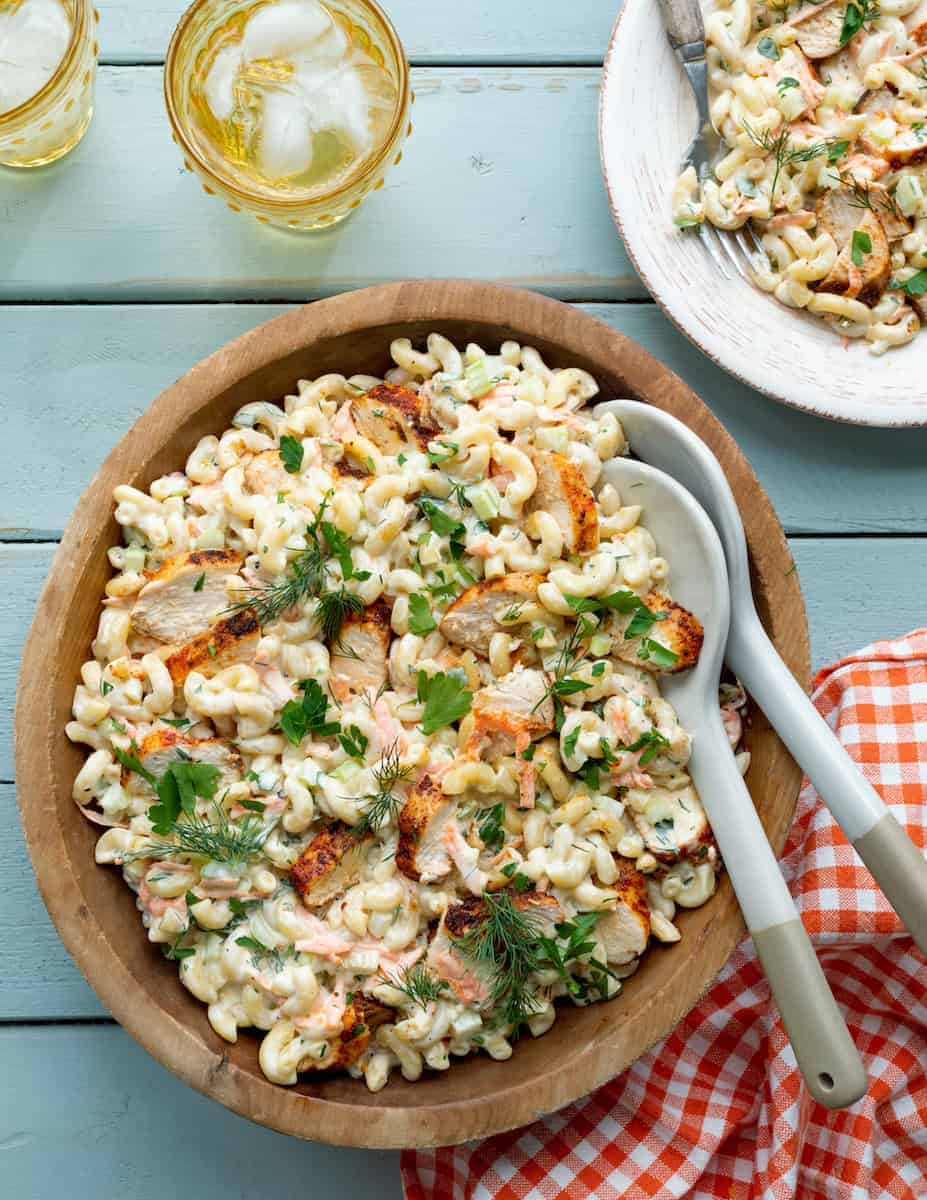 Creamy macaroni salad with chicken, shredded carrots, fresh herbs, and a creamy dressing in a wooden serving bowl with serving spoons.