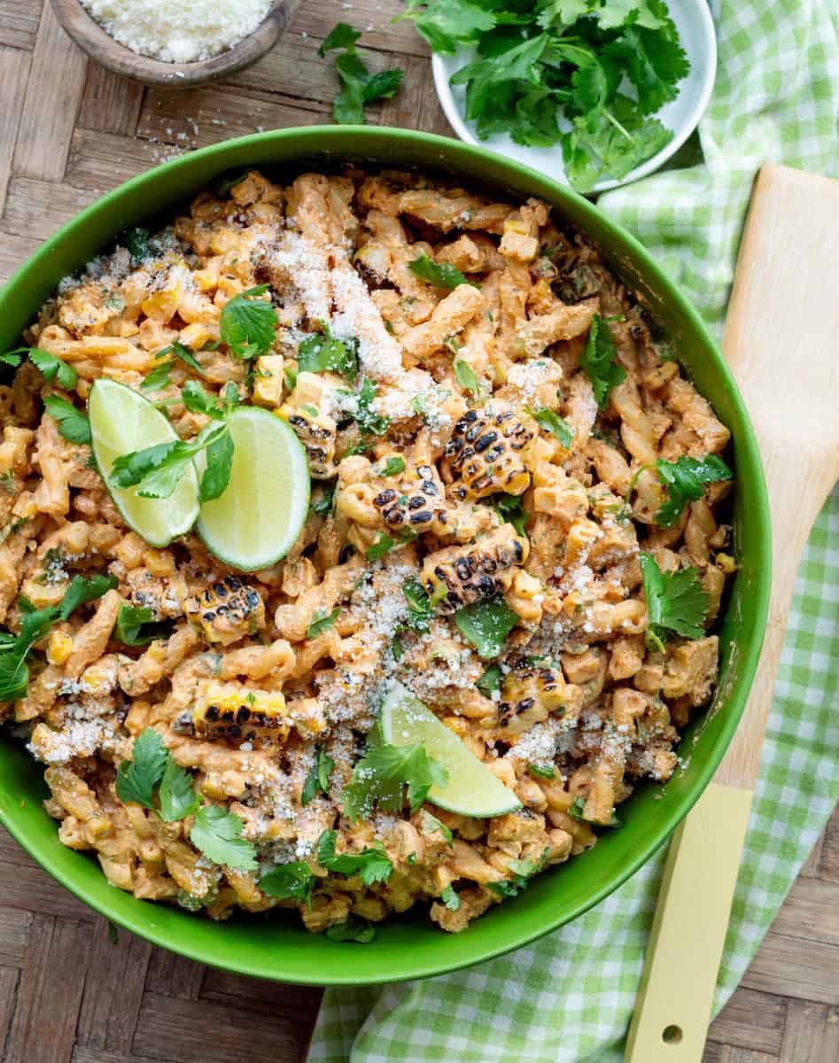 Creamy elote pasta salad served in a green bowl, garnished and topped with lime wedges.