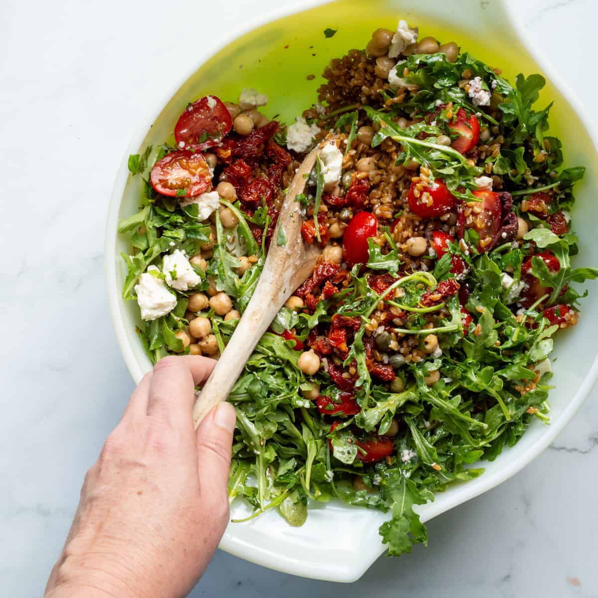 Stirring together the ingredients for Mediterranean farro salad in a large bowl.