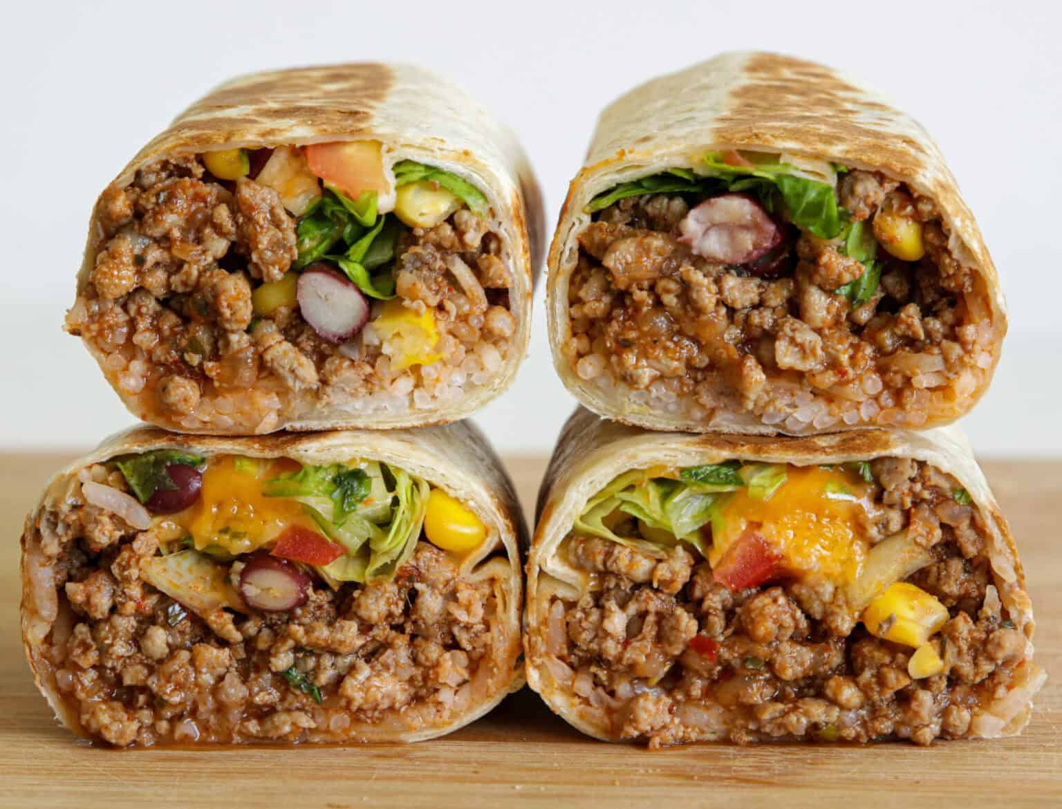Ground beef burritos cut in half and filled with seasoned beef, rice, vegetables, and melted cheese.
