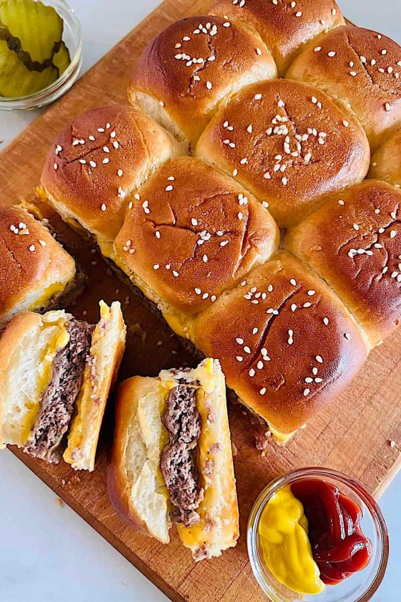 Cheeseburger sliders on soft rolls with beef patties and melted cheese, topped with sesame seeds.