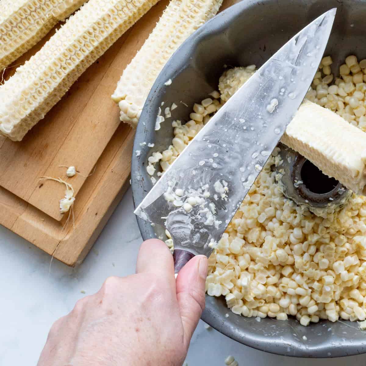 Scraping the corn milk from the cobs into a Bundt pan of fresh corn kernels.