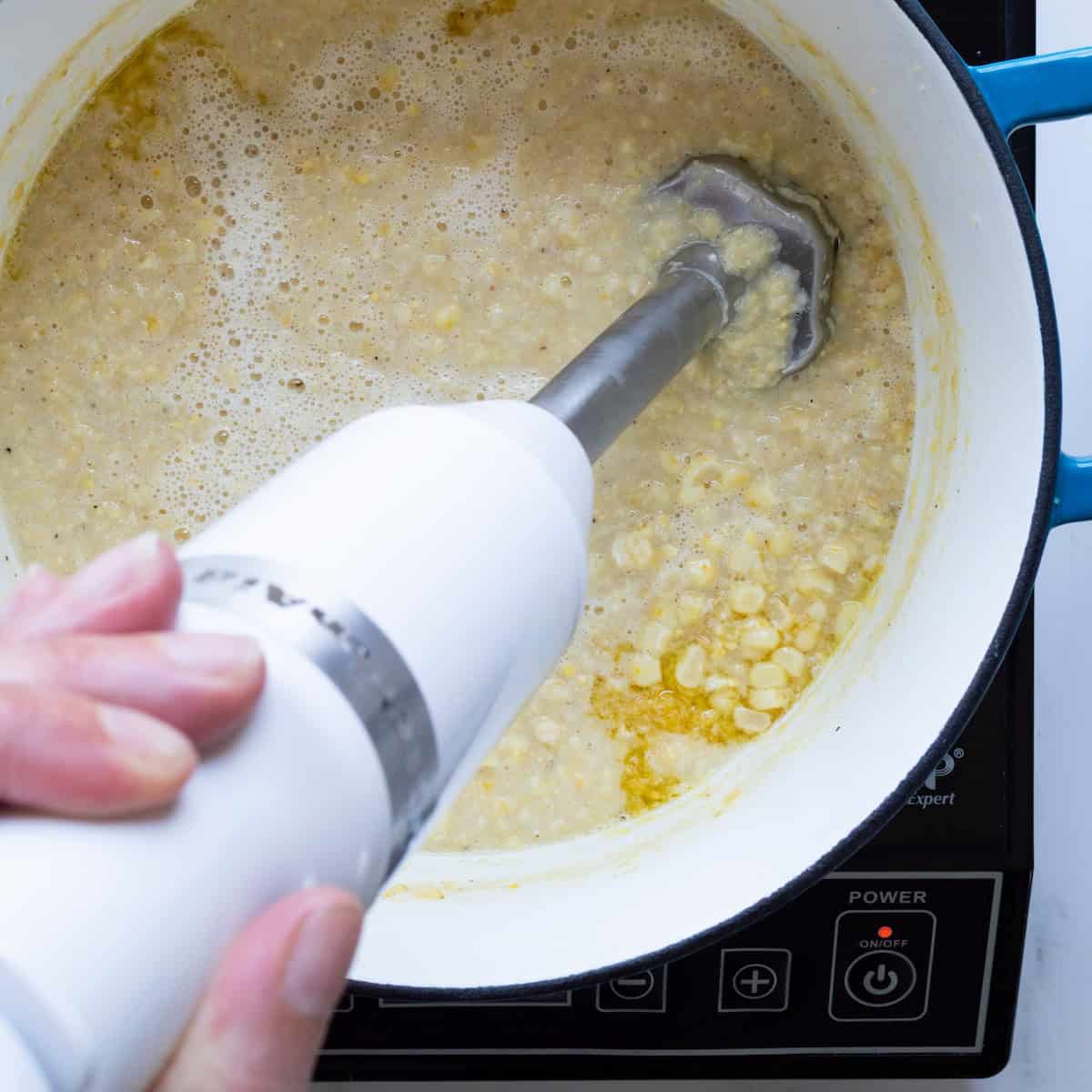 Blending the creamed corn using an immersion blender.