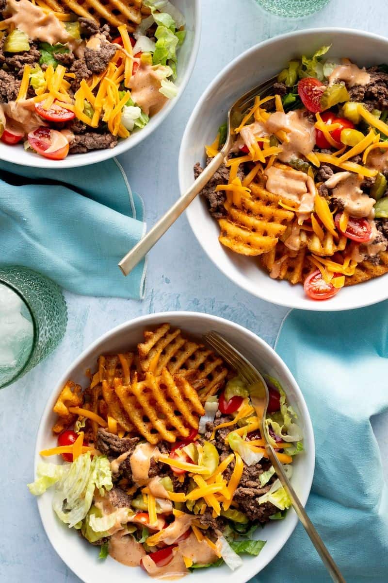 Hamburger bowls with ground beef, lettuce, tomatoes, pickles, shredded cheese, waffle fries, and creamy sauce.