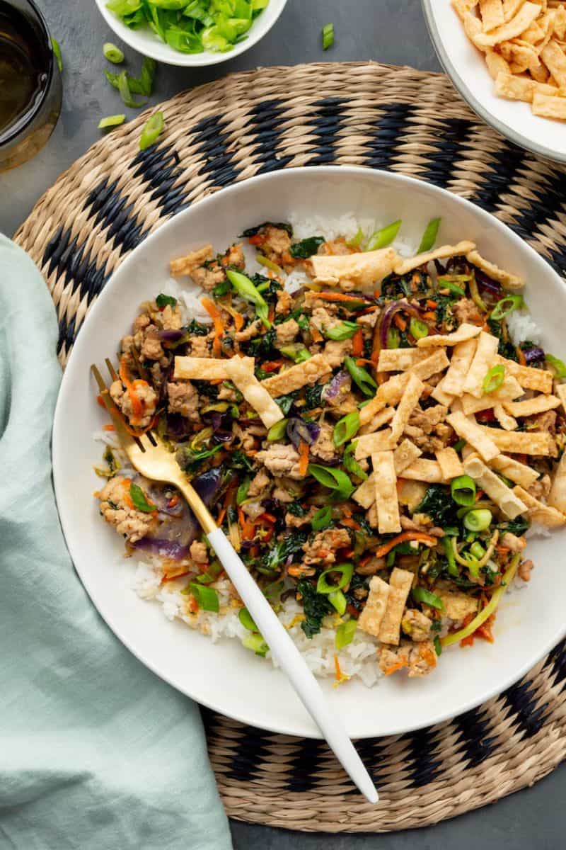 Egg roll bowl served over white rice with ground meat, mixed vegetables, green onions, and crispy strips.