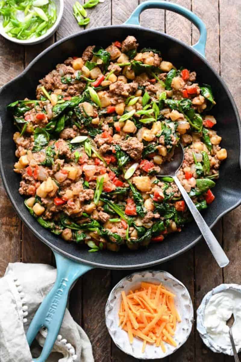 Skillet ground beef and potatoes with spinach, red peppers, and sliced green onions.