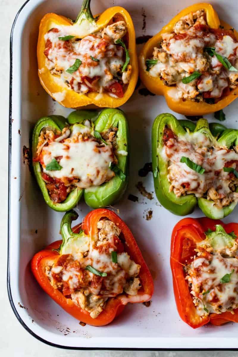 Ground turkey stuffed peppers topped with melted cheese and chopped herbs in a baking dish.