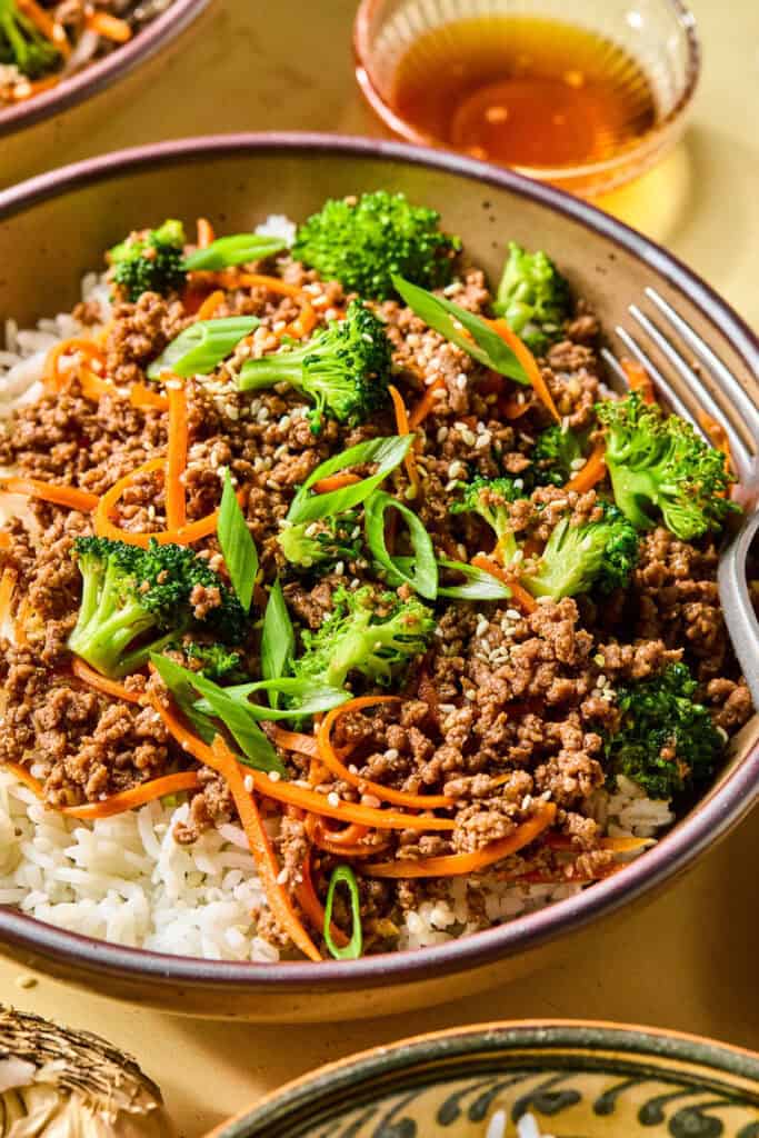 Honey garlic ground beef bowls served over rice with broccoli, shredded carrots, green onions, and sesame seeds.
