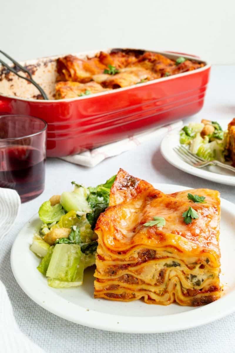 Meat lovers' lasagna with layers of pasta, meat sauce, and melted cheese served with a side salad.