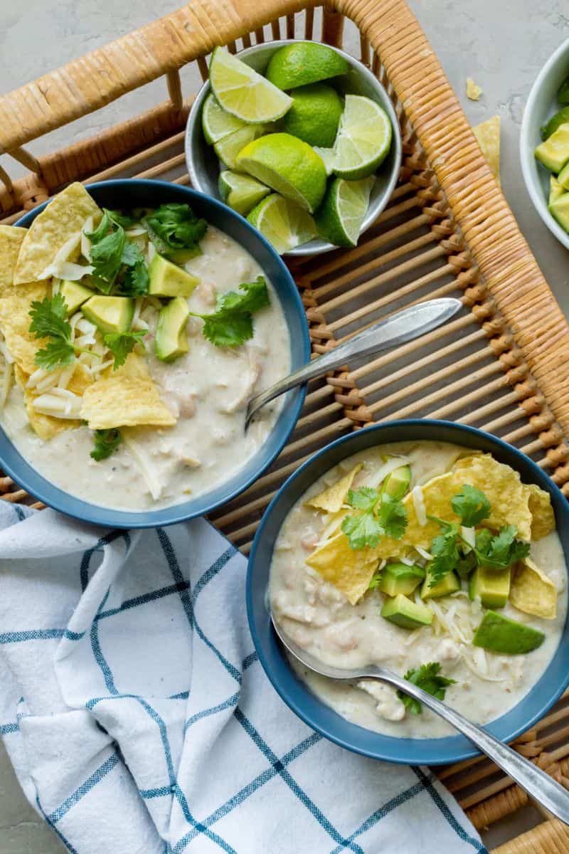 Instant Pot white turkey chili topped with avocado, shredded cheese, tortilla chips, cilantro, and lime.