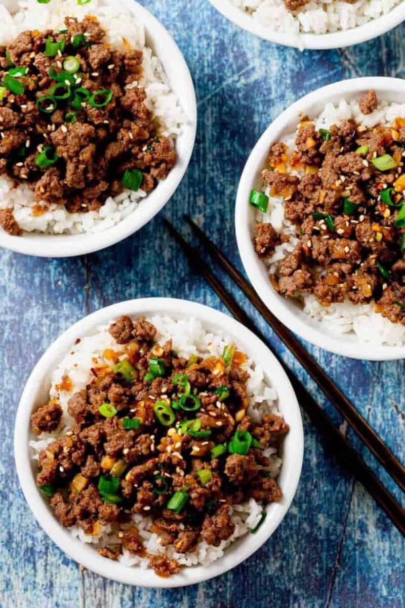 Korean beef bowl served over white rice with ground beef, green onions, sesame seeds, and chopped vegetables.