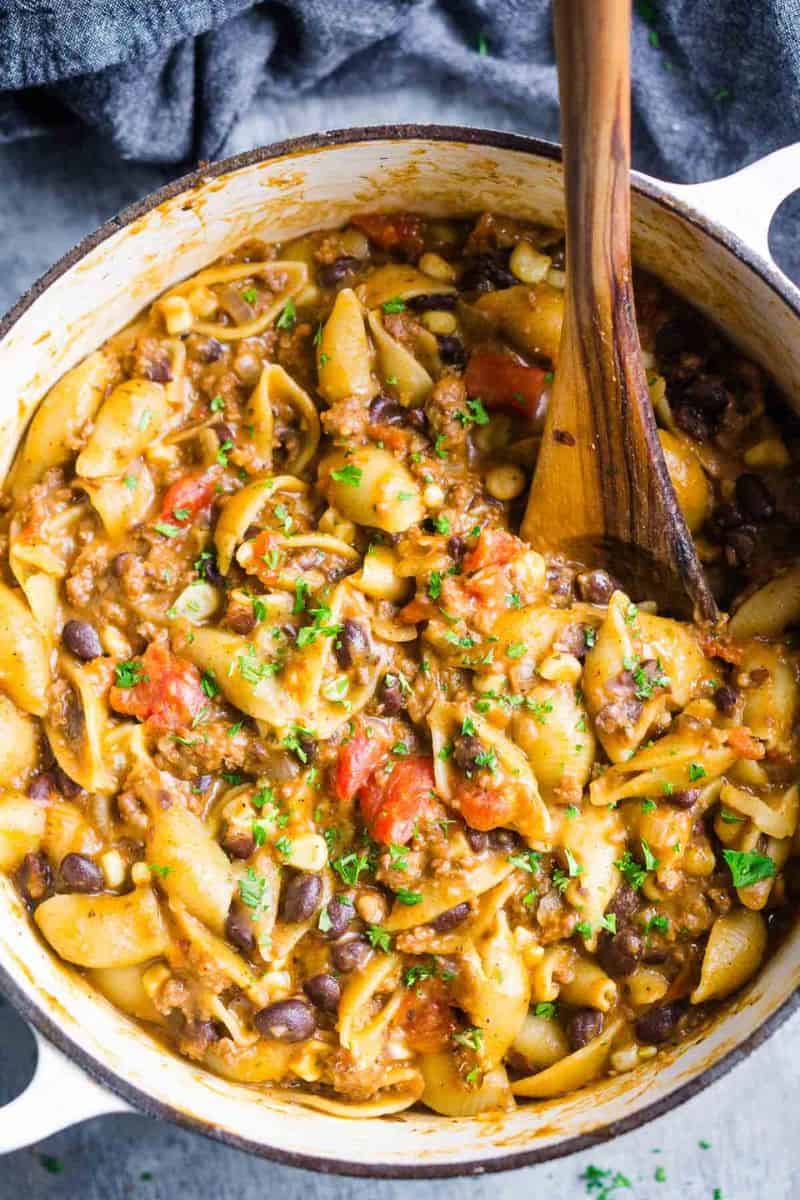 Easy taco pasta with pasta shells, ground beef, black beans, corn, tomatoes, and chopped herbs.