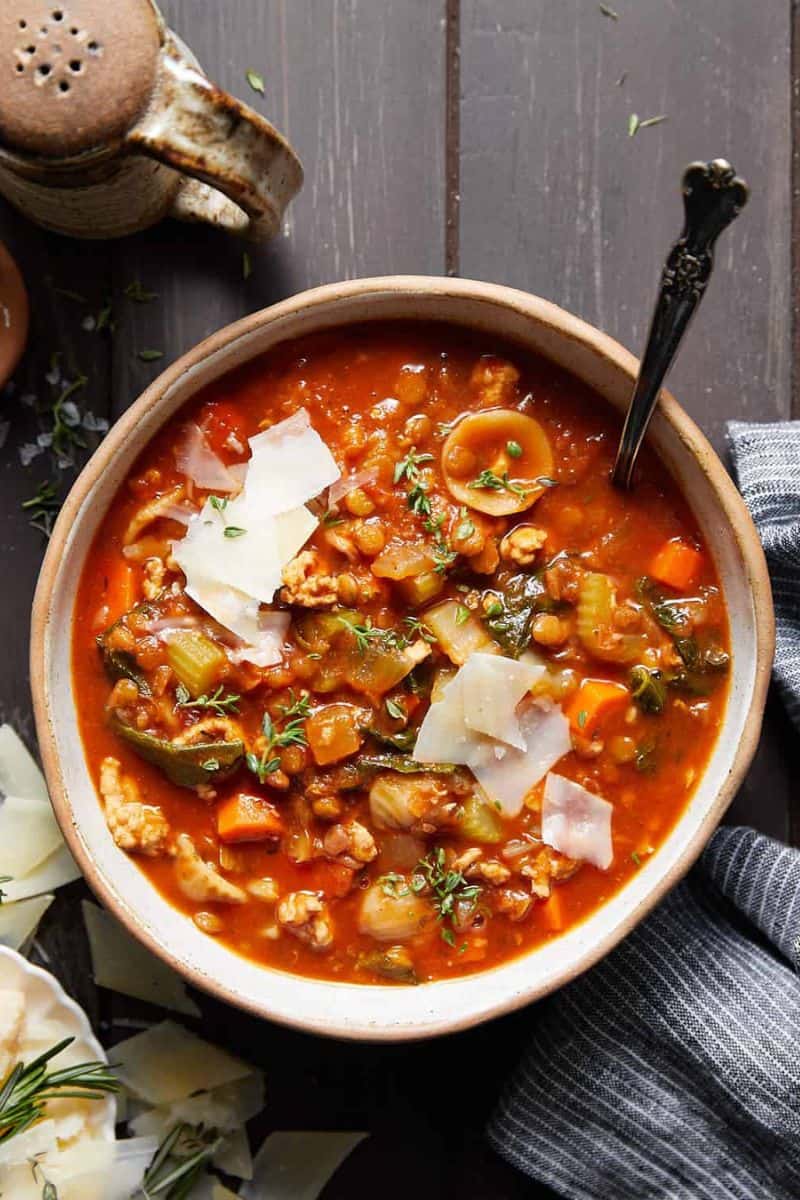 Turkey lentil soup served in a bowl with vegetables, lentils, shaved cheese, and fresh herbs.