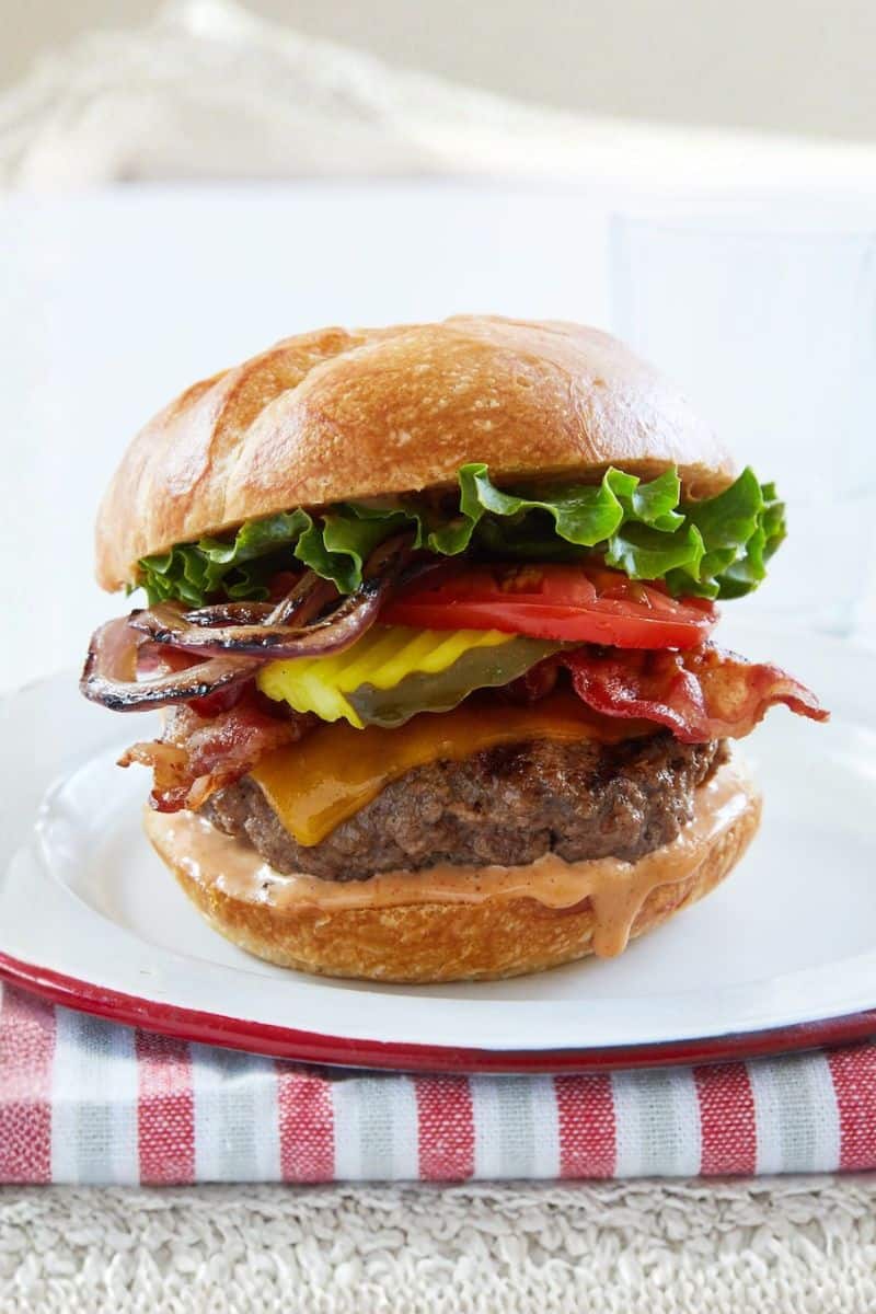 Ultimate cheeseburger stacked with a beef patty, melted cheese, bacon, pickles, tomato, lettuce, and onions on a bun.