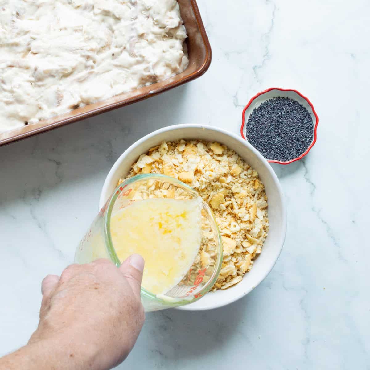 Pouring melted butter over crushed Ritz crackers in a white bowl.
