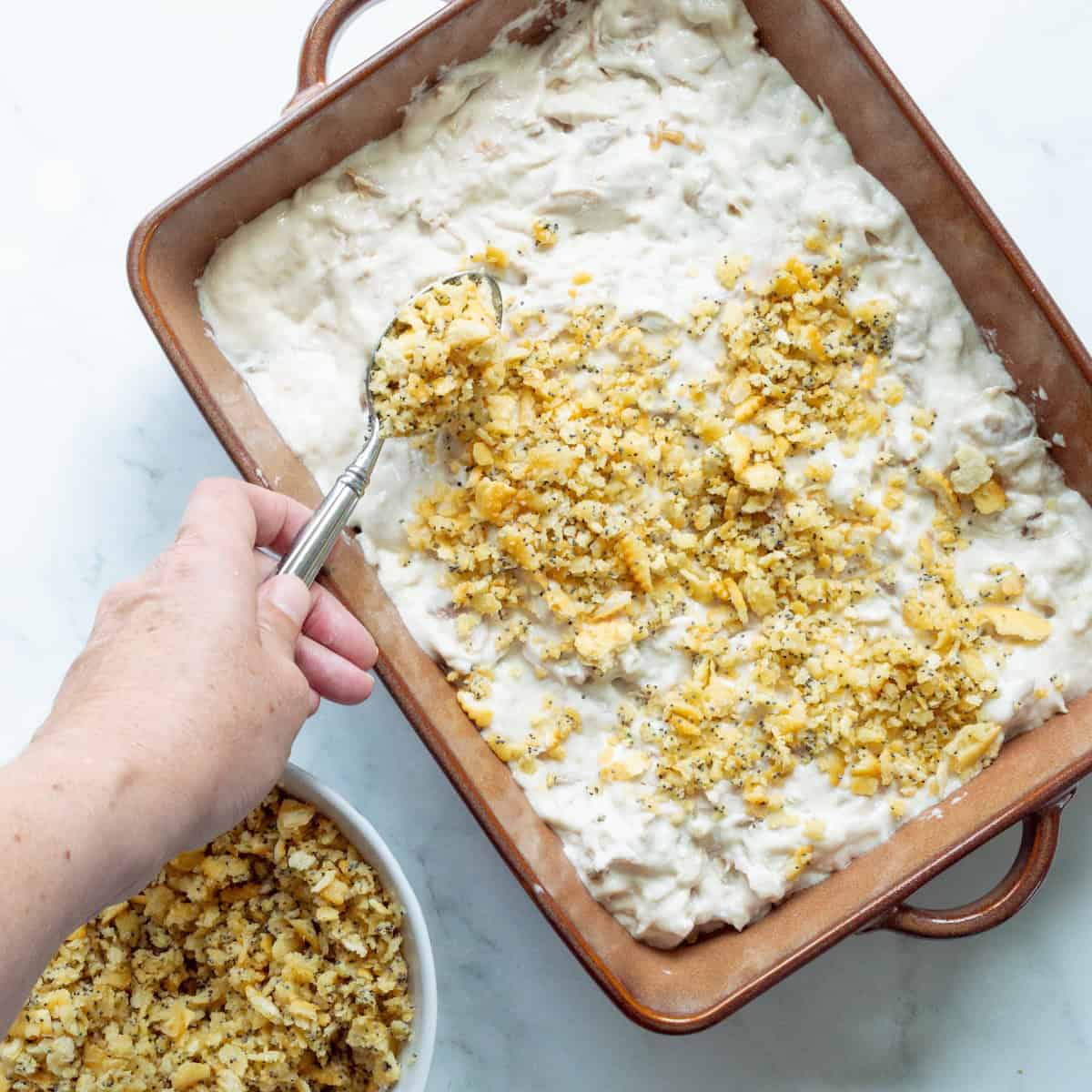 Sprinkling the Ritz cracker and poppyseed topping over the chicken filling.