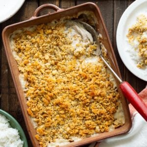 A brown casserole dish of poppyseed chicken with a serving on the side.