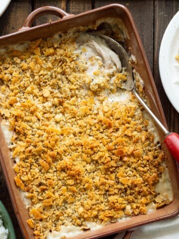 A brown casserole dish of poppyseed chicken with a serving on the side.