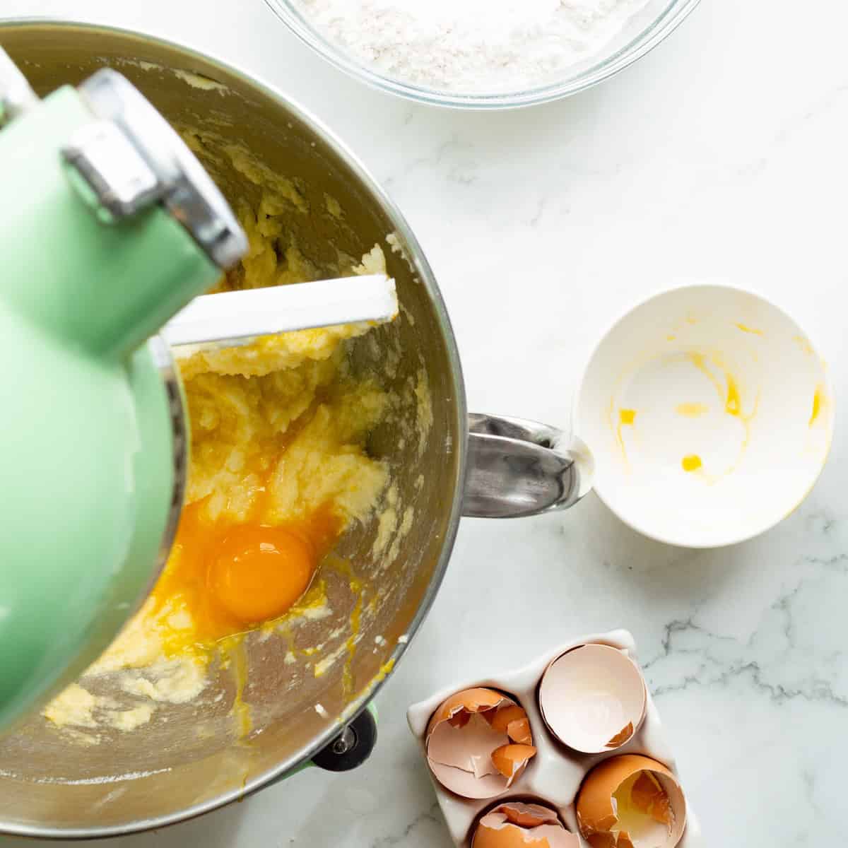 Adding eggs to creamed butter and sugar in a green mixer.