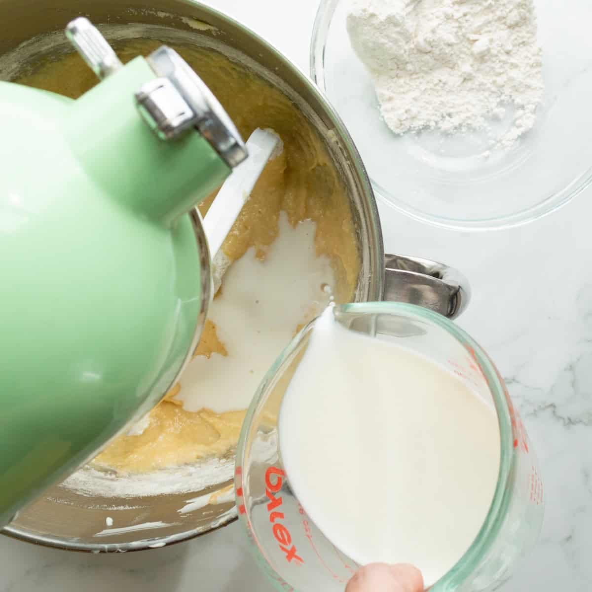 Pouring milk into the batter in a green mixer.
