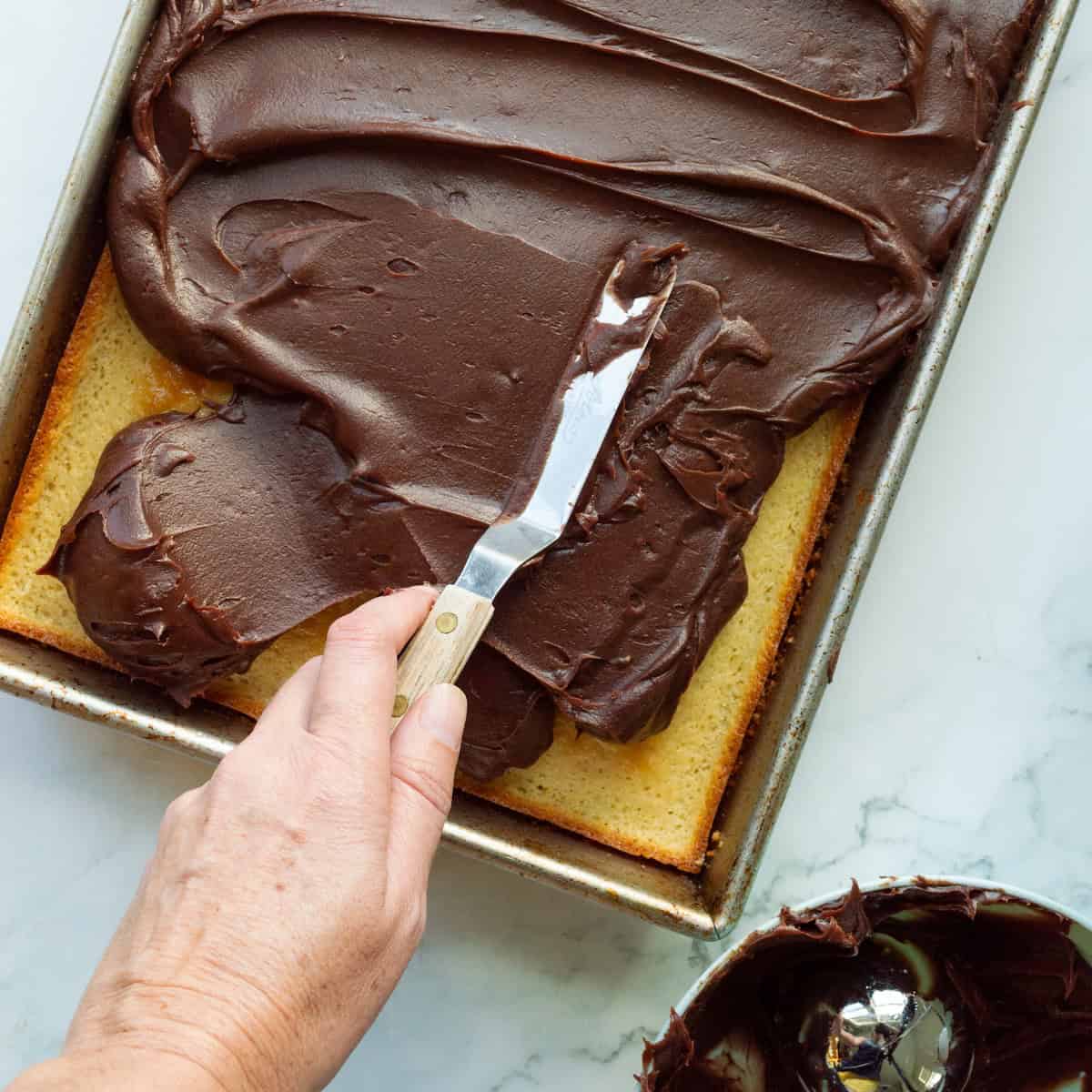 Spreading chocolate frosting onto yellow cake.