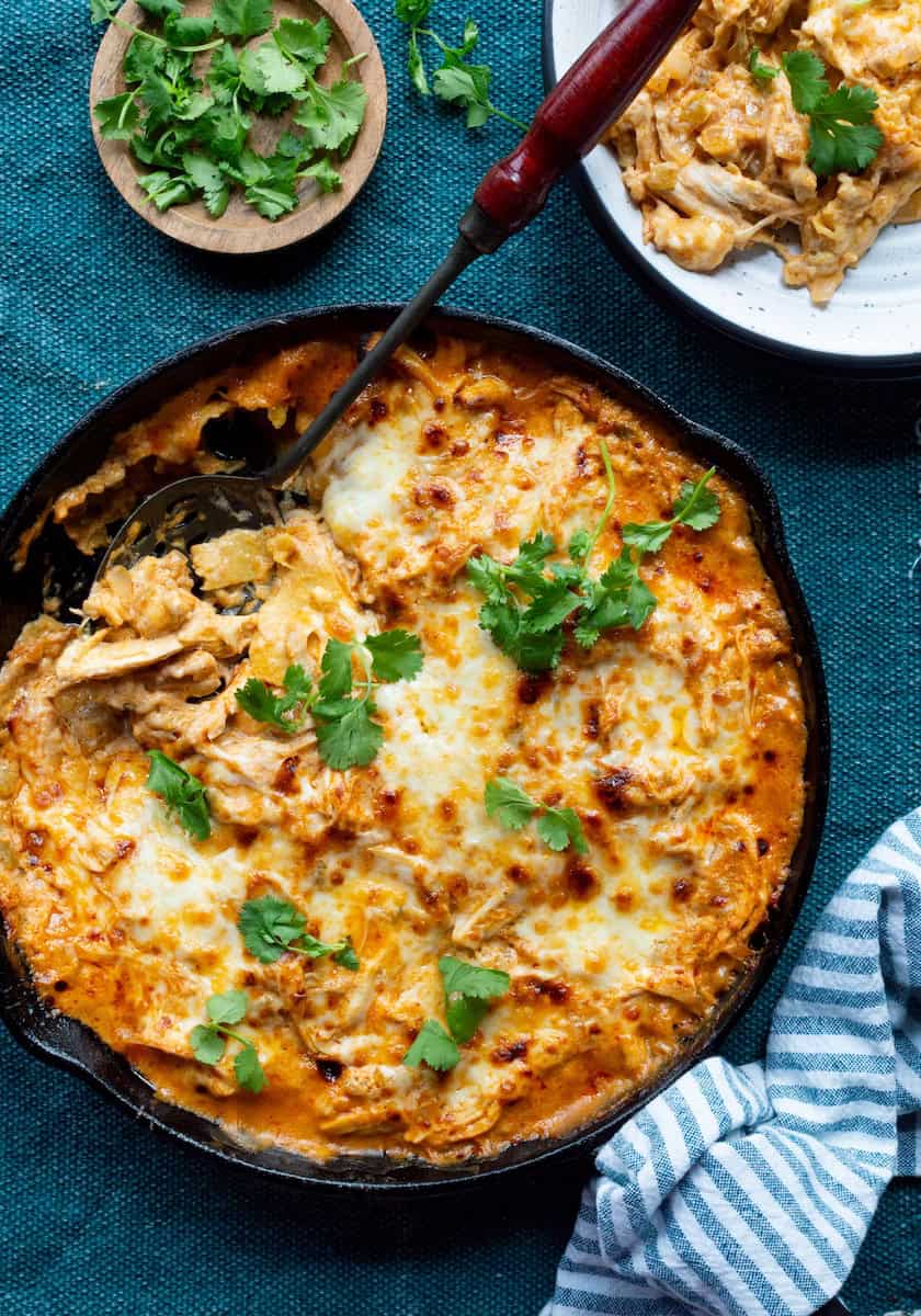 A cast-iron skillet of layered chicken and sour cream enchilada casserole.