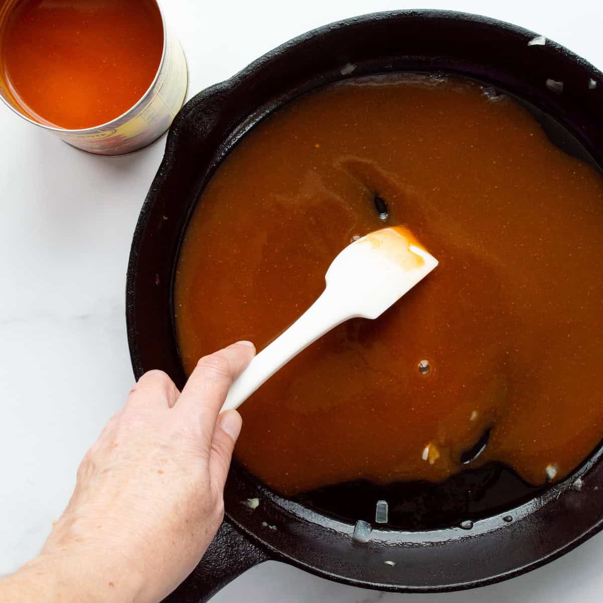 Spreading red enchilada sauce in the bottom of a cast iron skillet.