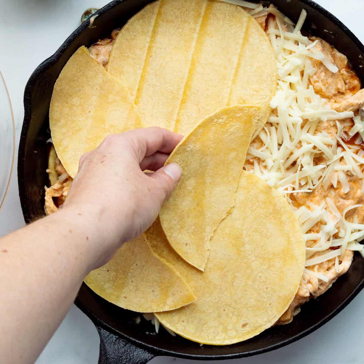 Layering the ingredients for sour cream chicken enchiladas in a cast-iron skillet.
