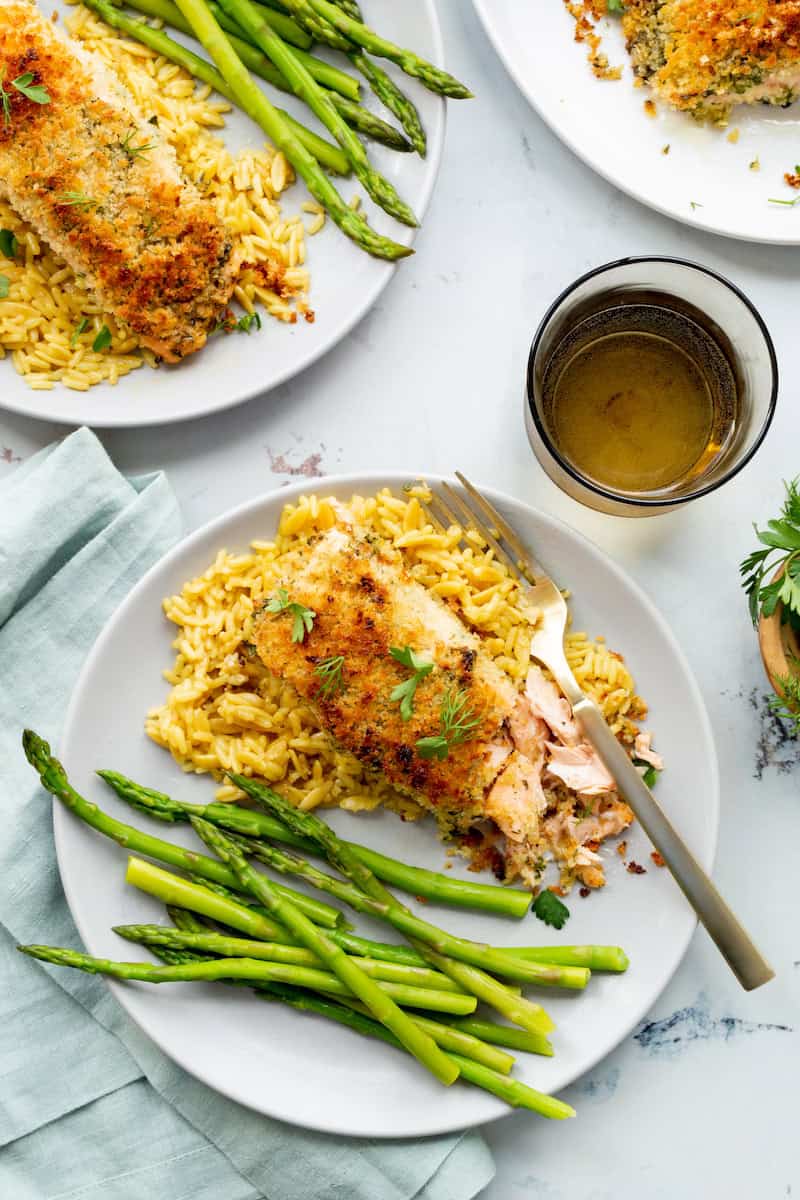 Norwegian salmon with panko herb crust served over golden rice with fresh asparagus, garnished with parsley and dill on a white dinner plate.