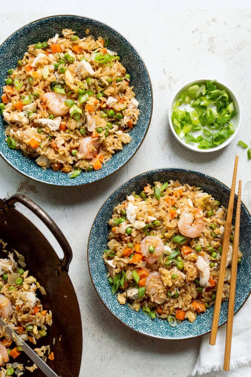 Better than takeout shrimp fried rice with chicken and vegetables, featuring shrimp, tender chicken, peas, carrots, and green onions in blue bowls.