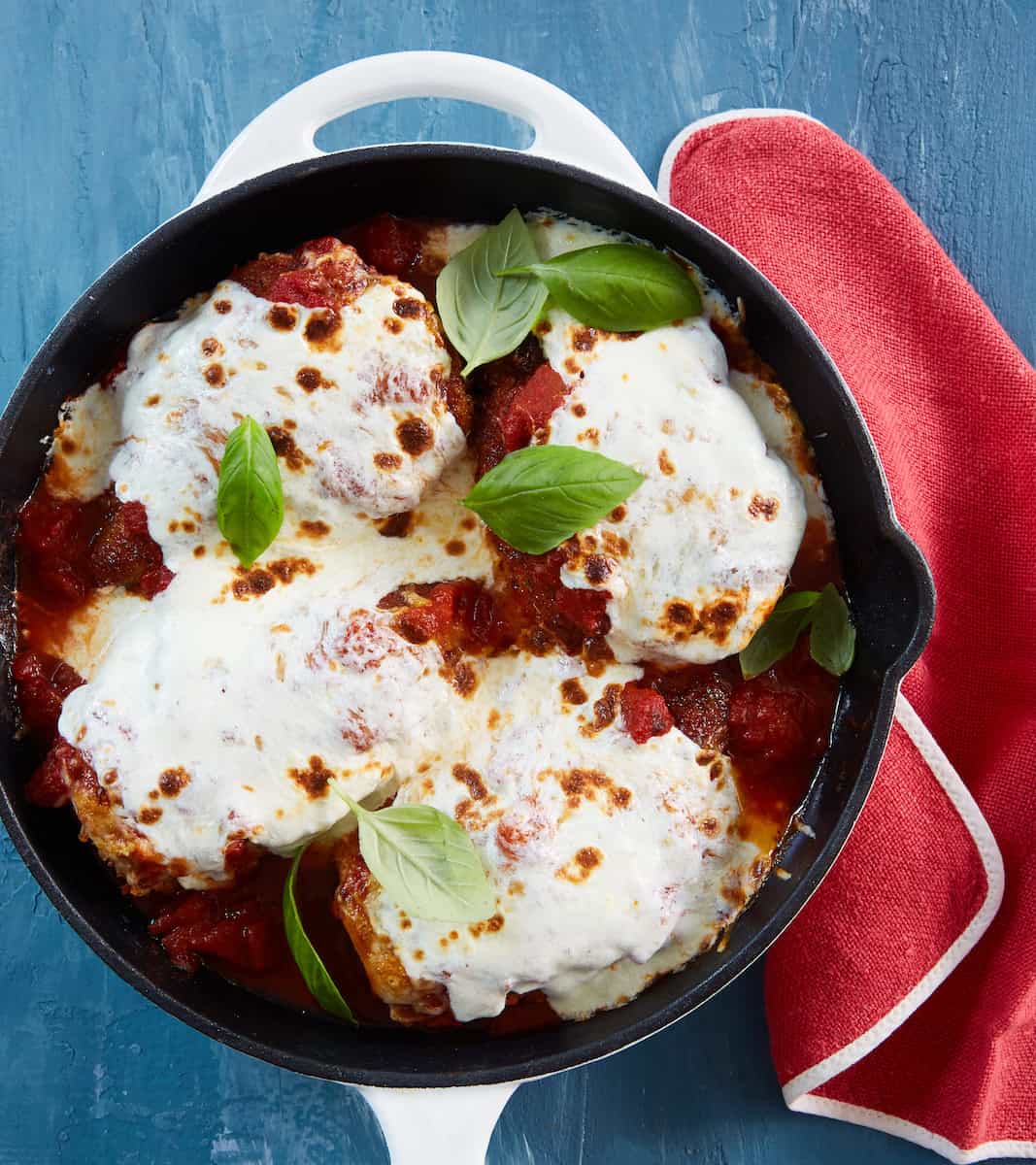 Cast iron chicken parm topped with melted mozzarella cheese, marinara sauce, and fresh basil leaves, served in a black cast iron skillet.