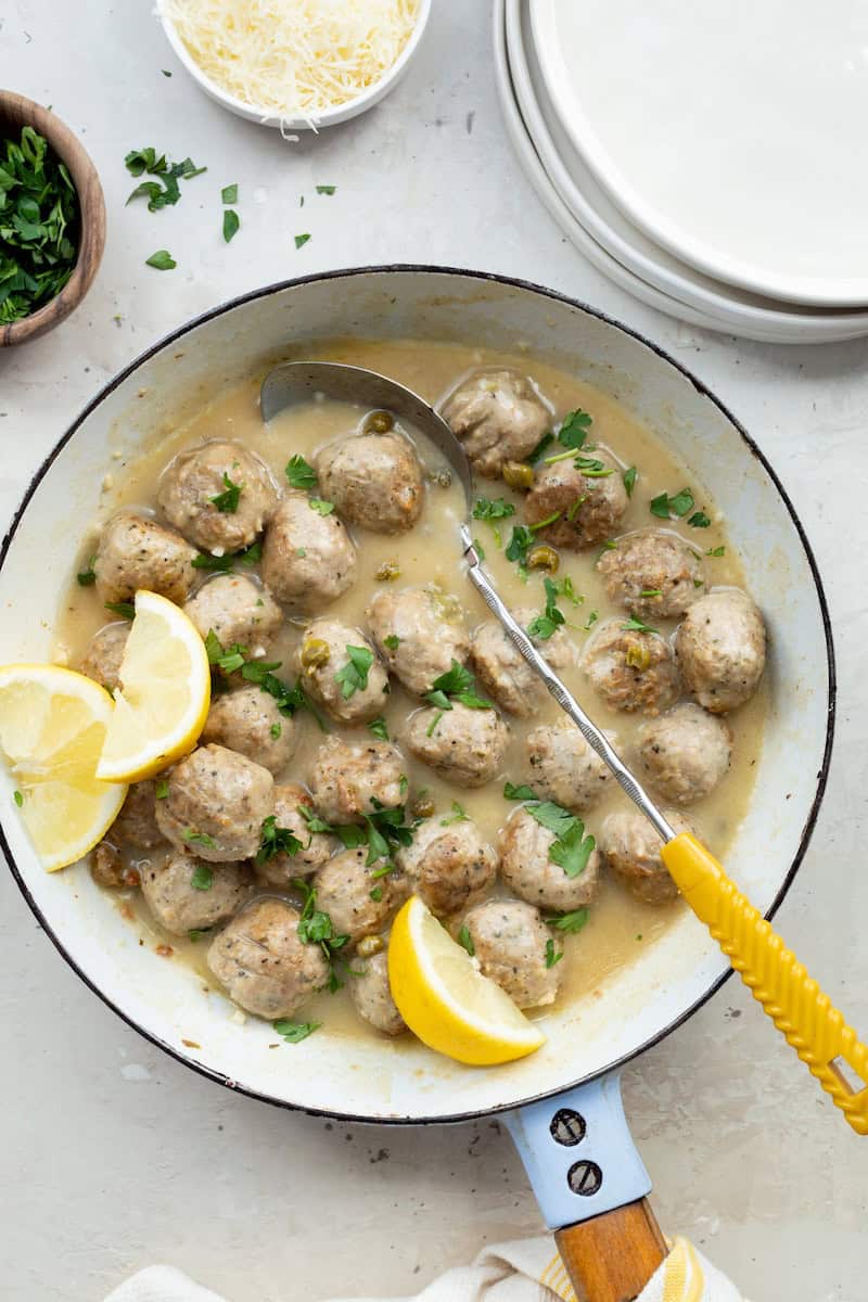 Trader Joe's chicken meatballs with piccata sauce, capers, lemon wedges, and fresh parsley served in a skillet with creamy lemon sauce.