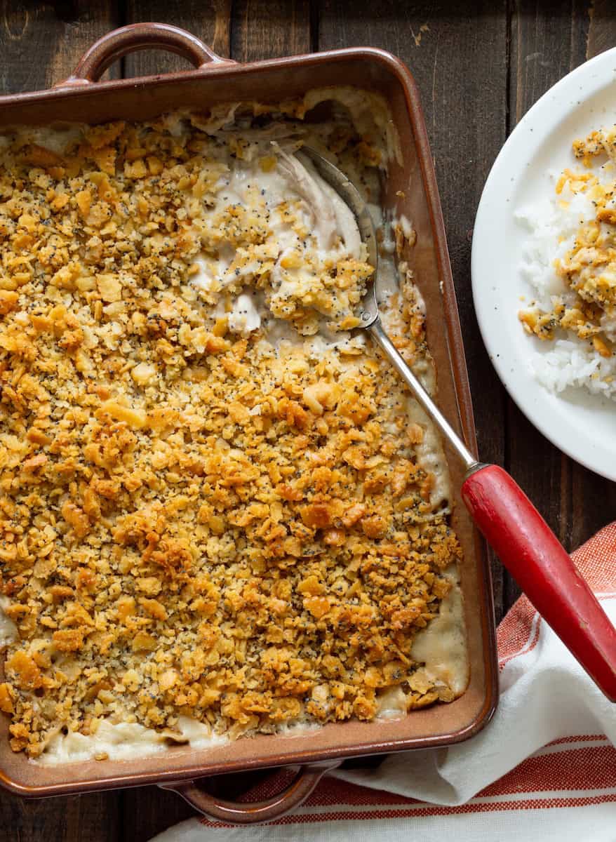 Poppy seed chicken casserole with creamy shredded chicken and a golden, buttery cracker topping, served in a baking dish with a side of rice.