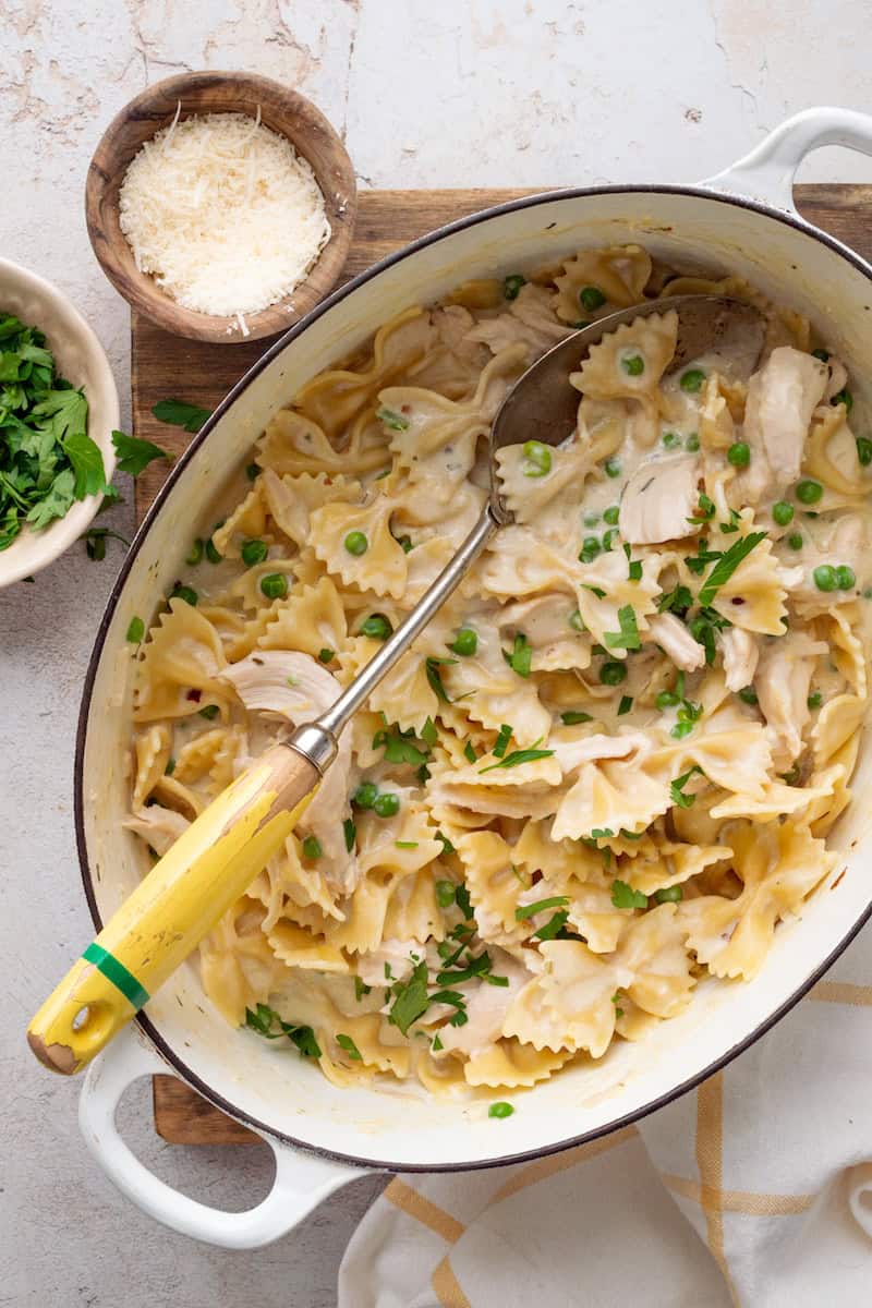 Lemon Boursin pasta with chicken and peas tossed in a creamy sauce, topped with fresh parsley and served in a white pot with a serving spoon.